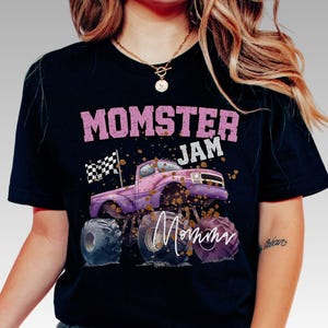 Pictured is a woman wearing a black t-shirt which says "MOMSTER JAM" in mauve pink color. There is a pink and purple monster truck with a checkered flag and a personalize signature name on the truck