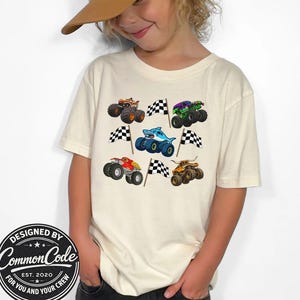Boy in a natural cream colored t-shirt with various monster truck vehicles in cartoon style with racing checkered flags . Monster trucks jam themed with digger truck, shark megalodon truck, tiger shark truck, bull toro truck and dragon truck. Perfect for race day, monster truck birthday parties, kids gift, matching mommy daddy and mini shirts. Comes in Baby, toddler, kid, teen and adult sizes. Very colorful and vibrant fun graphic style shirt.