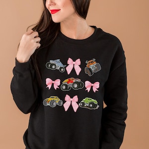 woman model is wearing a black monster truck jam Girls Woman's Sweatshirt with 5 monster trucks and 4 Pink Coquette Bows Long-Sleeve Sweaters: Family Matching Long-sleeved monster truck shirts outfits. Adult, teen, youth, toddler and infant sizes.