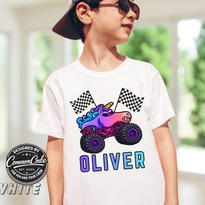 Pictured is a boy wearing a white t-shirt with large blue rainbow colored sparkle smash unicorn monster truck with 2 black and white checkered flags and custom name OLIVER