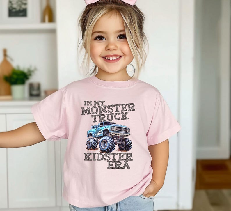 Puede incluir: Una camiseta rosa con un gr&aacute;fico de cami&oacute;n monstruo azul y el texto "In My Monster Truck Kidster Era".