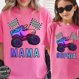 Pictured is Mother and daughter wearing berry pink comfort colors tee's with blue rainbow sparkle smash unicorn monster trucks with 2 black and white checkered flags above custom name MAMA and SOPHIA