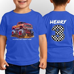 Peut inclure: T-shirt bleu &agrave; manches courtes avec un motif de monster truck rouge, des d&eacute;tails &agrave; carreaux noirs et blancs et le texte "A LITTLE DIRT DOESN'T HURT." Le dos affiche le nom "HENRY" au-dessus d'un grand chiffre "3" &agrave; motif &agrave; carreaux.