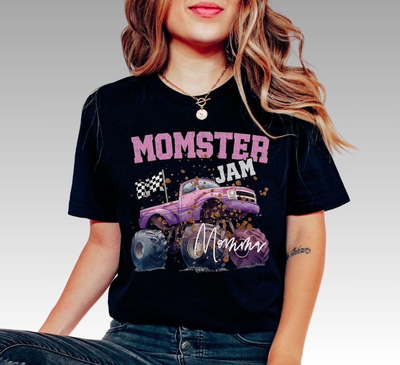 Pictured is a woman wearing a black t-shirt which says "MOMSTER JAM" in mauve pink color. There is a pink and purple monster truck with a checkered flag and a personalize signature name on the truck