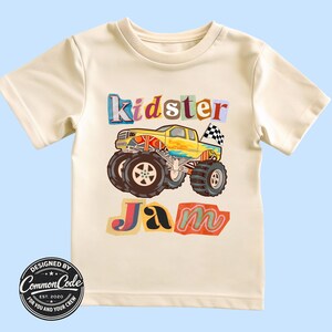 Puede incluir: Camiseta color crema con un gr&aacute;fico de cami&oacute;n monstruo colorido y las palabras "Kidster Jam". El dise&ntilde;o incluye un cami&oacute;n amarillo, neum&aacute;ticos negros grandes y una bandera a cuadros. La camiseta tambi&eacute;n tiene el texto "Designed by Common Code, Est. 2020."
