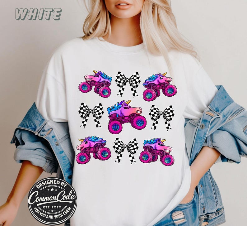 May include: White t-shirt featuring a repeating pattern of pink monster trucks with unicorn horns and black and white checkered bows. The word "WHITE" is at the top. Designed by Common Code.