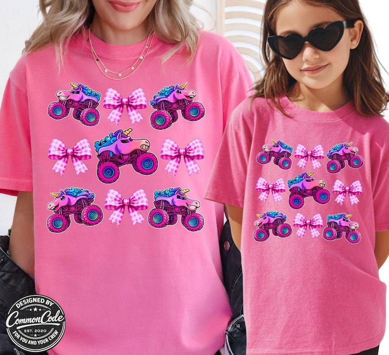 May include: Pink t-shirts with a repeating pattern of a unicorn monster truck and pink bows. The shirts are worn by a woman and a child. The text "DESIGNED BY Common Code EST. 2020 FOR YOU AND YOUR CREW" is visible.
