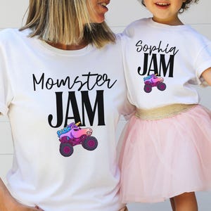 May include: White t-shirts with matching designs. One shirt says "Momster JAM" and the other says "Sophia JAM". Both shirts feature a colorful monster truck with a unicorn design. The child is wearing a pink tutu.