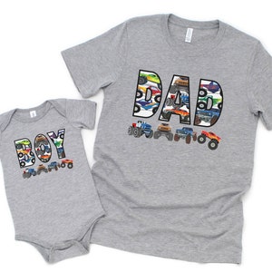 Custom T-shirt in light gray with monster truck theme. personalized name in big white letters filled with images of monster trucks - the large one says DAD, the baby bodysuit says BOY but you can have any name you wish