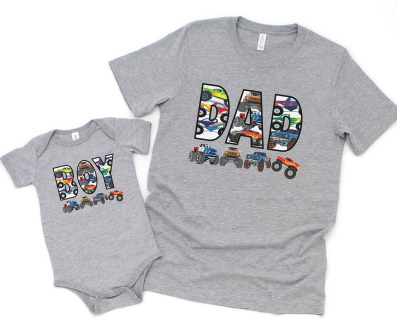 Custom T-shirt in light gray with monster truck theme. personalized name in big white letters filled with images of monster trucks - the large one says DAD, the baby bodysuit says BOY but you can have any name you wish