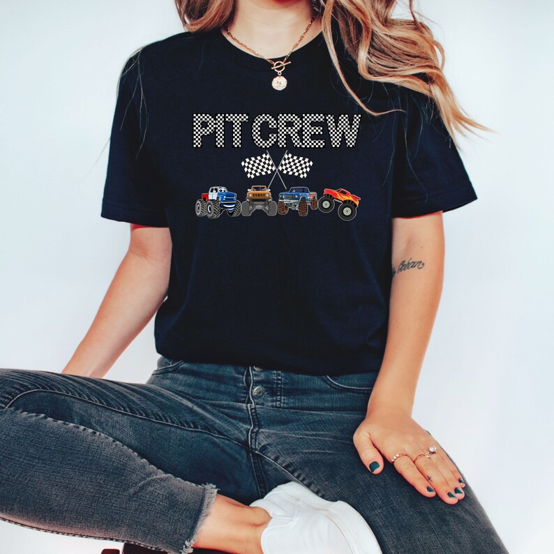 Puede incluir: Camiseta negra con el texto "PT CREW" en blanco con un dise&ntilde;o de bandera a cuadros. Cuatro monster trucks est&aacute;n alineados debajo del texto.
