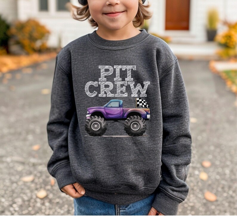 Puede incluir: Sudadera gris oscuro con las palabras "PIT CREW" en letras blancas. Un cami&oacute;n monstruo morado con neum&aacute;ticos negros grandes y una bandera a cuadros est&aacute; impreso en la parte delantera. La sudadera est&aacute; hecha de un material suave y c&oacute;modo.