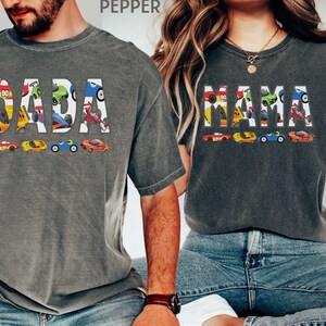 May include: Two gray t-shirts with the words "DADA" and "MAMA" spelled out in colorful cartoon race cars.