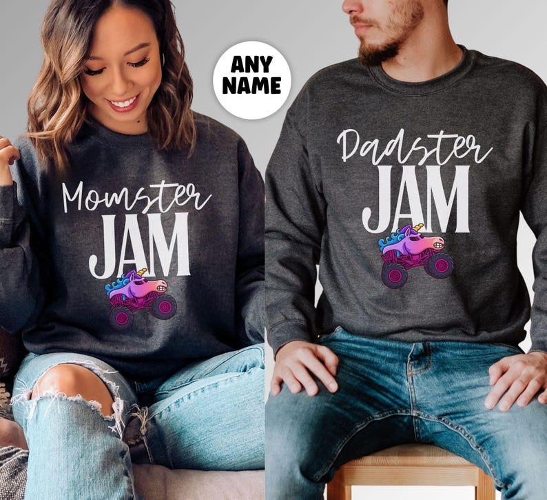 May include: Two dark gray sweatshirts with the text "Momster JAM" and "Dadster JAM" in white. Each sweatshirt features a colorful monster truck with a unicorn design. The sweatshirts are worn with blue jeans.