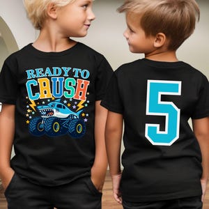 Ready To Crush Young Boy with bright colored shark monster truck graphic with stars and lightning bolts on the front of shirt and a Big Custom Number 5 on the back to match