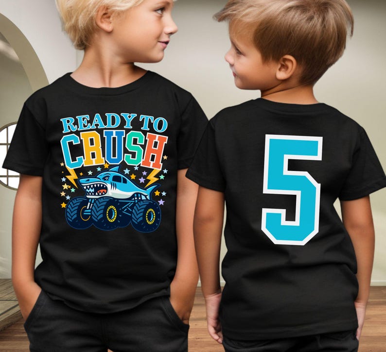 Ready To Crush Young Boy with bright colored shark monster truck graphic with stars and lightning bolts on the front of shirt and a Big Custom Number 5 on the back to match