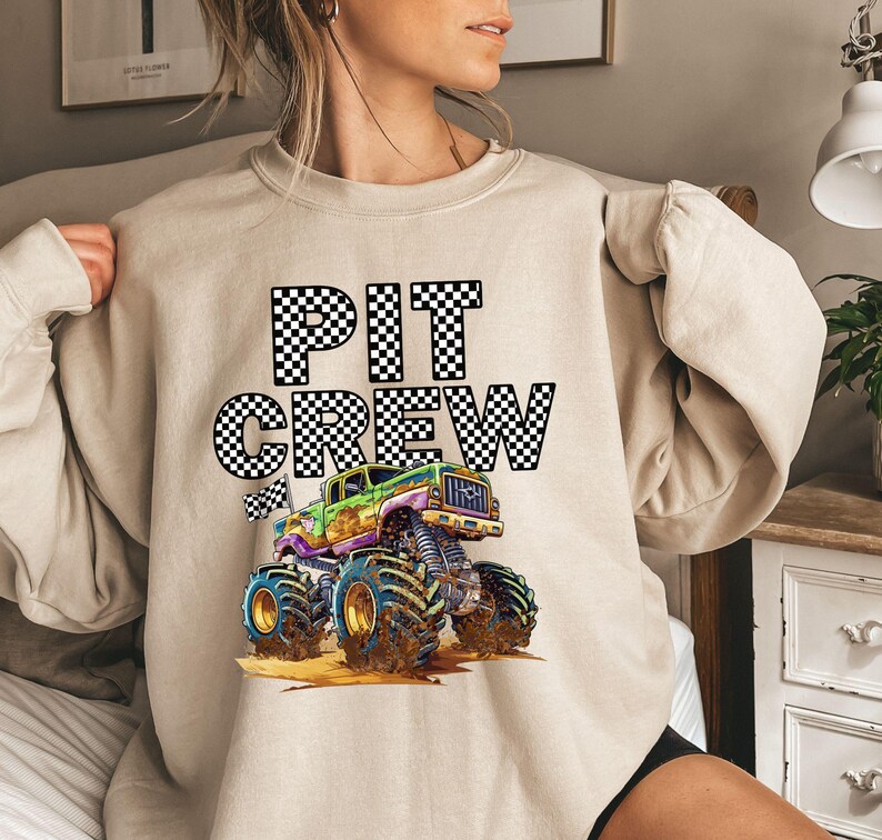 May include: A beige sweatshirt with a black and white checkered graphic that says "PIT CREW" and a cartoon monster truck with green, yellow, and black details.