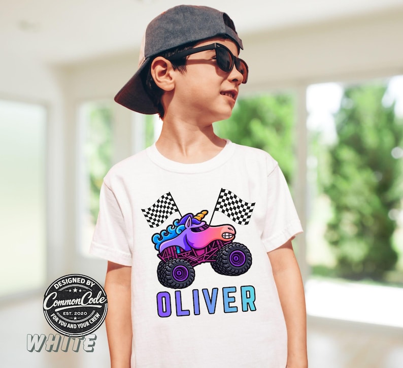Pictured is a boy wearing a white t-shirt with large blue rainbow colored sparkle smash unicorn monster truck with 2 black and white checkered flags and custom name OLIVER