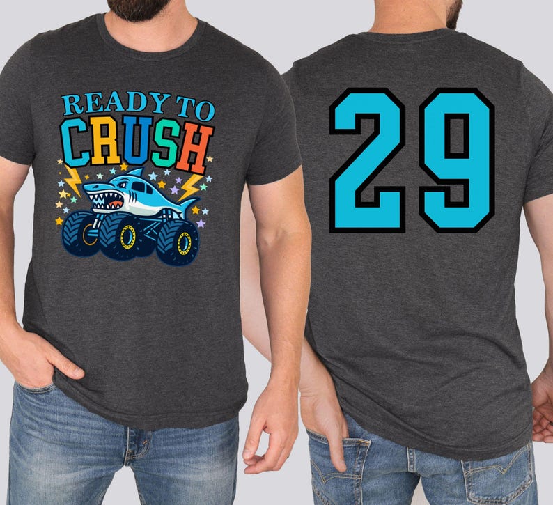 Dad's dark gray t-shirt with a shark monster truck graphic and the text "READY TO CRUSH" on the front. The back of the shirt features the number "29" in turquoise with a black outline. The shirt is made of a soft material.