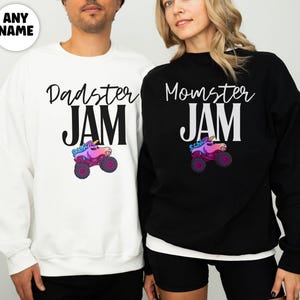 May include: White and black sweatshirts with the text "Dadster JAM" and "Momster JAM" in a script font. Each sweatshirt features a colorful monster truck graphic. The sweatshirts are worn by two people.