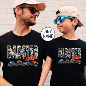 father son models are wearing matching black t-shirts that are monster truck themed. "pattern letters that say "Dadster Jam" and "Kidster Jam". Each top has a row of 4 Monster Trucks underneath the letters.