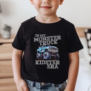 Puede incluir: Una camiseta negra con un gr&aacute;fico de cami&oacute;n monstruo azul y el texto "In My Monster Truck Kidster Era".