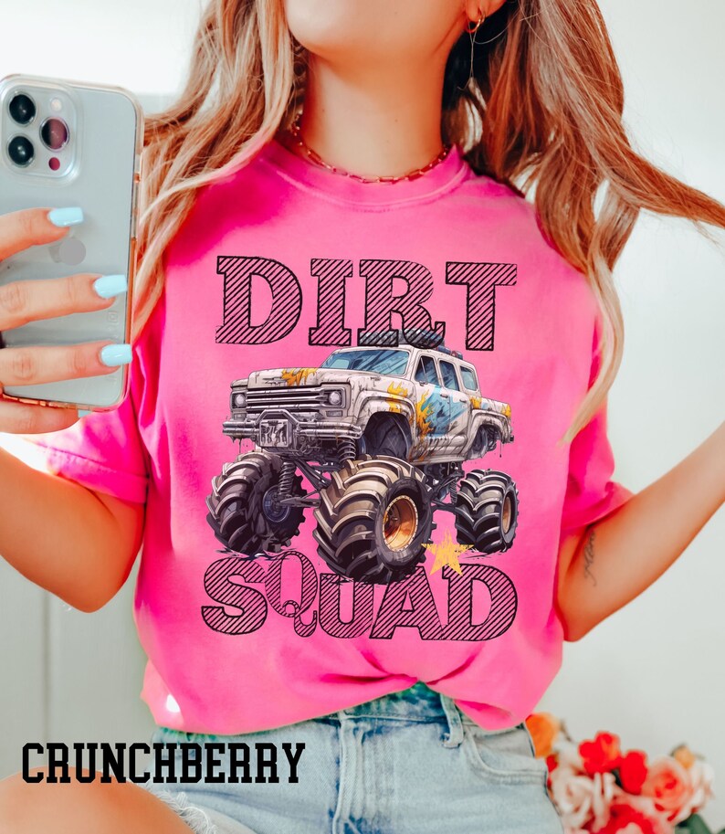 Puede incluir: Una camiseta rosa brillante con las palabras "DIRT SQUAD" y un gr&aacute;fico de un monster truck. El texto y el dise&ntilde;o del cami&oacute;n son en negro. La palabra "CRUNCHBERRY" est&aacute; impresa en la parte inferior de la camiseta.