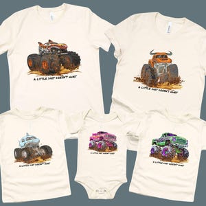 Off-white t-shirts and a onesie featuring colorful monster truck designs. Each shirt has a different truck design, including a shark, bull, and a truck with a flame design. The text "A LITTLE DIRT DOESN'T HURT" is printed below each truck.