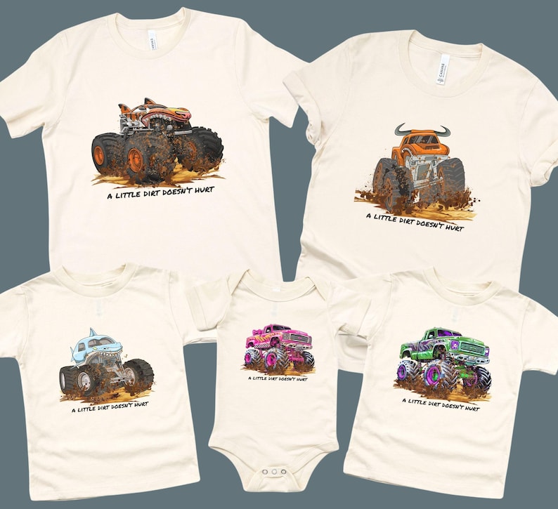 Off-white t-shirts and a onesie featuring colorful monster truck designs. Each shirt has a different truck design, including a shark, bull, and a truck with a flame design. The text "A LITTLE DIRT DOESN'T HURT" is printed below each truck.