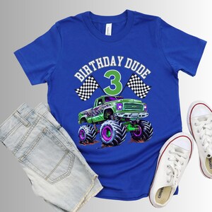 May include: Blue t-shirt with a graphic of a green monster truck, the text "BIRTHDAY DUDE 3", and checkered flags. The shirt is paired with denim shorts and white sneakers.