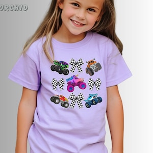 May include: A light purple t-shirt featuring colorful monster truck graphics and checkered bows. The trucks are in various colors, including green, orange, red, blue, and pink. The word "ORCHID" is in the upper left corner.