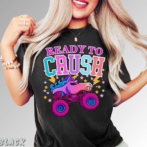 May include: Black t-shirt with the text "READY TO CRUSH" in pink, blue, and white. The graphic features a cartoon unicorn monster truck in pink, purple, and blue, with stars and lightning bolts.