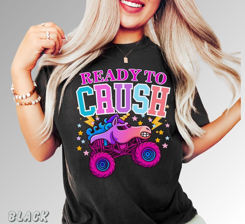 May include: Black t-shirt with the text "READY TO CRUSH" in pink, blue, and white. The graphic features a cartoon unicorn monster truck in pink, purple, and blue, with stars and lightning bolts.