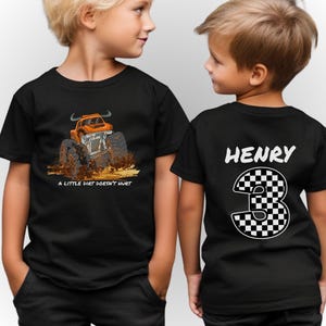 Peut inclure: T-shirts noirs avec un dessin de monster truck et le texte "A Little Dirt Doesn't Hurt". Le dos d'un t-shirt affiche le nom "HENRY" et le chiffre 3 en damier.