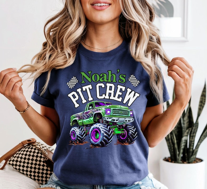 Woman is wearing a navy blue comfort colors T-shirt which says Noah's PIT CREW in green and white letters with a big green and purple monster truck graphic and 2 checkered flags
