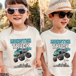 May include: Two children wearing white t-shirts with a blue monster truck graphic and the text "Monster Truck Jam". The girl's shirt says "Allie" and the boy's shirt says "Noah".