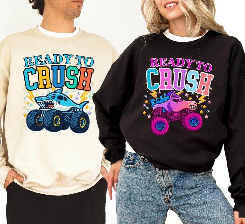 Pu&ograve; includere: Felpe beige e nere con la scritta "READY TO CRUSH". La felpa beige presenta un design di monster truck a forma di squalo, mentre la felpa nera ha un design di monster truck a forma di unicorno. Entrambe le felpe hanno grafiche colorate.