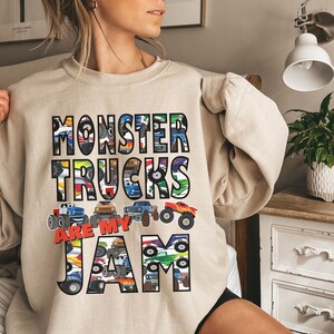 Puede incluir: Una sudadera beige con un dise&ntilde;o gr&aacute;fico de monster trucks. El texto en la sudadera dice "Monster Trucks Are My Jam".