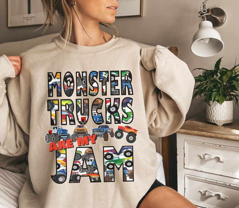 Puede incluir: Una sudadera beige con un dise&ntilde;o gr&aacute;fico de monster trucks. El texto en la sudadera dice "Monster Trucks Are My Jam".