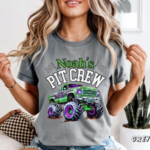 Pode incluir: Camiseta cinza com um gr&aacute;fico de um monster truck verde com rodas roxas e pretas. O texto "Noah's PIT CREW" est&aacute; acima do caminh&atilde;o em verde e branco. Bandeiras quadriculadas est&atilde;o em ambos os lados do texto.