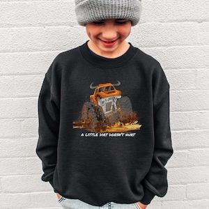 Op de afbeelding: Zwart sweatshirt met een oranje monster truck illustratie en de tekst "A LITTLE DIRT DOESN'T HURT". De afbeelding toont de truck in de modder. Het sweatshirt is gemaakt van een zacht materiaal.