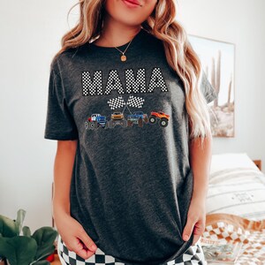 Puede incluir: Una camiseta gris oscuro con la palabra "MAMA" en fuente de cuadros blancos y negros. La palabra est&aacute; centrada en la camiseta y est&aacute; rodeada de cuatro monster trucks con banderas a cuadros.