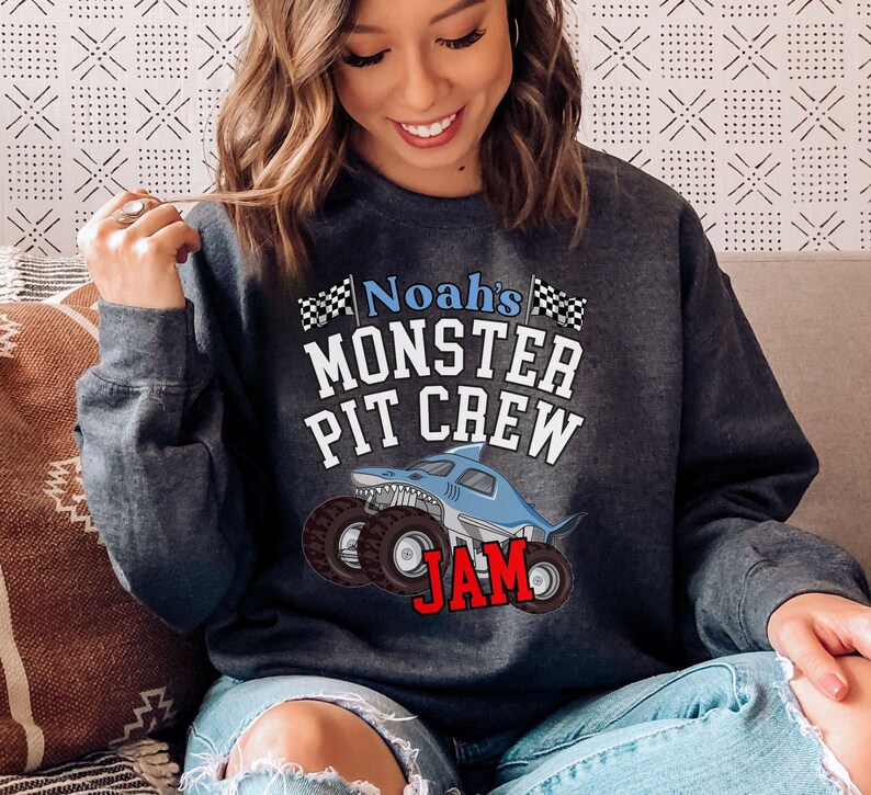 May include: Dark gray sweatshirt with the text "Noah's MONSTER PIT CREW JAM" in white, blue, and red. The design features a cartoon shark monster truck with large tires and checkered flags.