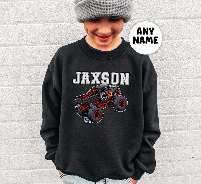 以下が含まれることがあります： 白いブロック文字で「JAXSON」という名前と、赤と黒のディテールが施された漫画のモンスタートラックが特徴の黒いスウェットシャツ。 トラックは大きな赤いホイールとスカルグラフィックを備えています。