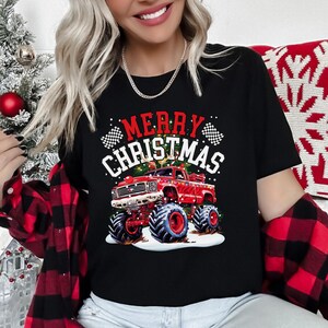 May include: Black t-shirt with a red monster truck graphic and the words "MERRY CHRISTMAS" in white and red. The truck has large tires and is decorated with Christmas lights. The shirt is a festive holiday design.