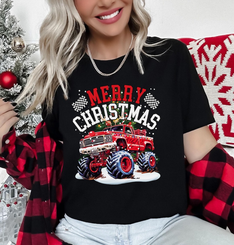May include: Black t-shirt with a red monster truck graphic and the words "MERRY CHRISTMAS" in white and red. The truck has large tires and is decorated with Christmas lights. The shirt is a festive holiday design.
