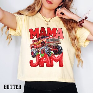 May include: A yellow t-shirt with a red monster truck graphic and the text "Mama Jam" in red and pink letters. The monster truck has a red body, black wheels, and yellow flames. The letters are surrounded by red strawberries.