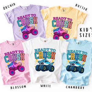 May include: Five colorful t-shirts with the text "READY TO CRUSH" and graphic designs. The shirts are in orchid, butter, blossom, white, and chambray. The designs include a unicorn monster truck and a shark monster truck.