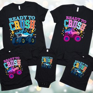 Pode incluir: T-shirts pretas e um body com o texto "READY TO CRUSH" e gr&aacute;ficos de monster truck. Os monster trucks s&atilde;o em v&aacute;rias cores, incluindo azul, rosa e roxo. As camisas s&atilde;o para tamanhos diferentes.