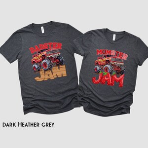 Op de afbeelding: Twee donkergrijze t-shirts met een monstertruck-afbeelding en de tekst "DADSTER JAM" en "MOMSTER JAM". Het woord "JAM" is gemaakt van aardbeien.